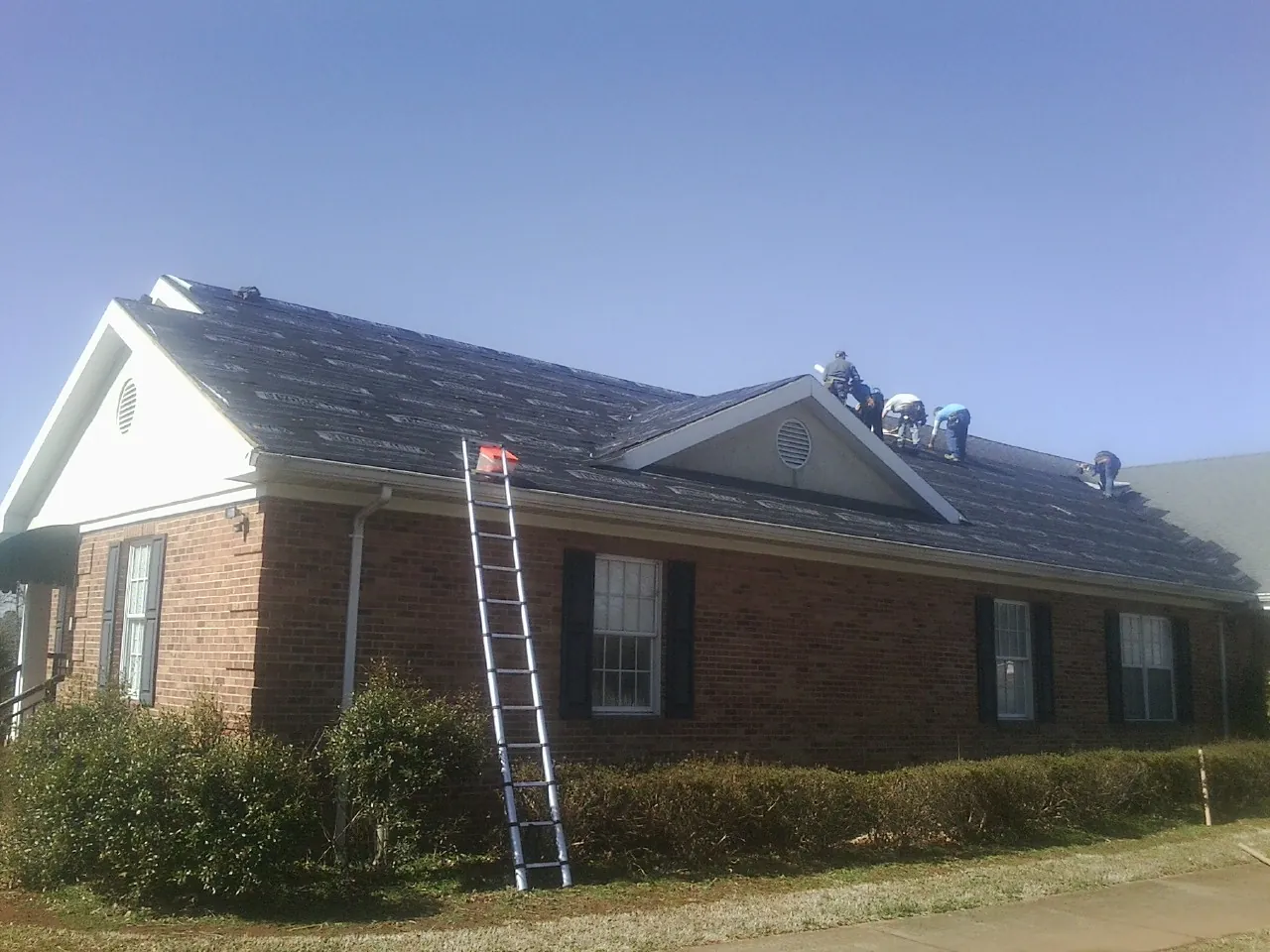 Crew tearing shingles off a brick ranch roof with a ladder set — Emergency Roof Repair work by our crew in Moroni