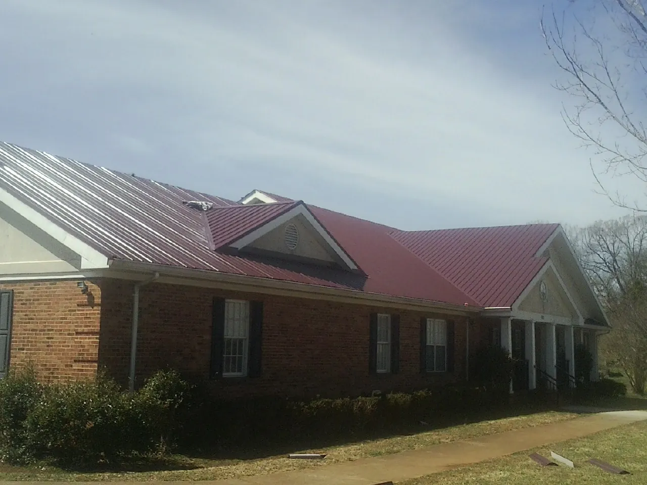 Red metal roof with gabled entries on a long brick building, from a Hail Damage Roof Repair job in Moroni