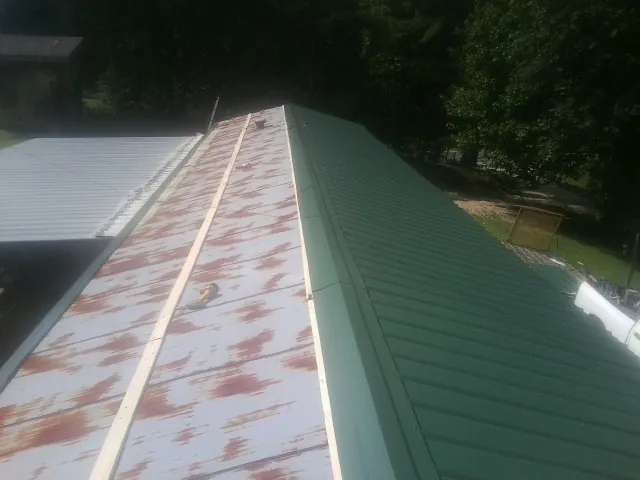 Old rusted panels beside newly installed green metal roofing — Wind Damage Roof Repair by Roofing Brothers in Moroni