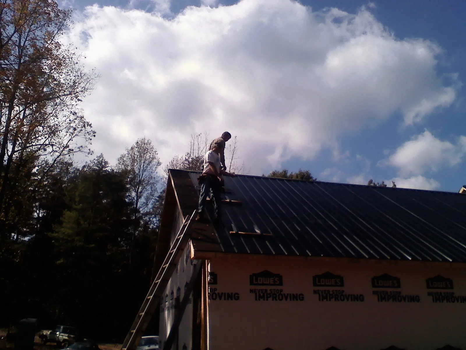 Roofer fastening dark metal panels high against a cloudy sky, from a Roof Inspection job in Moroni