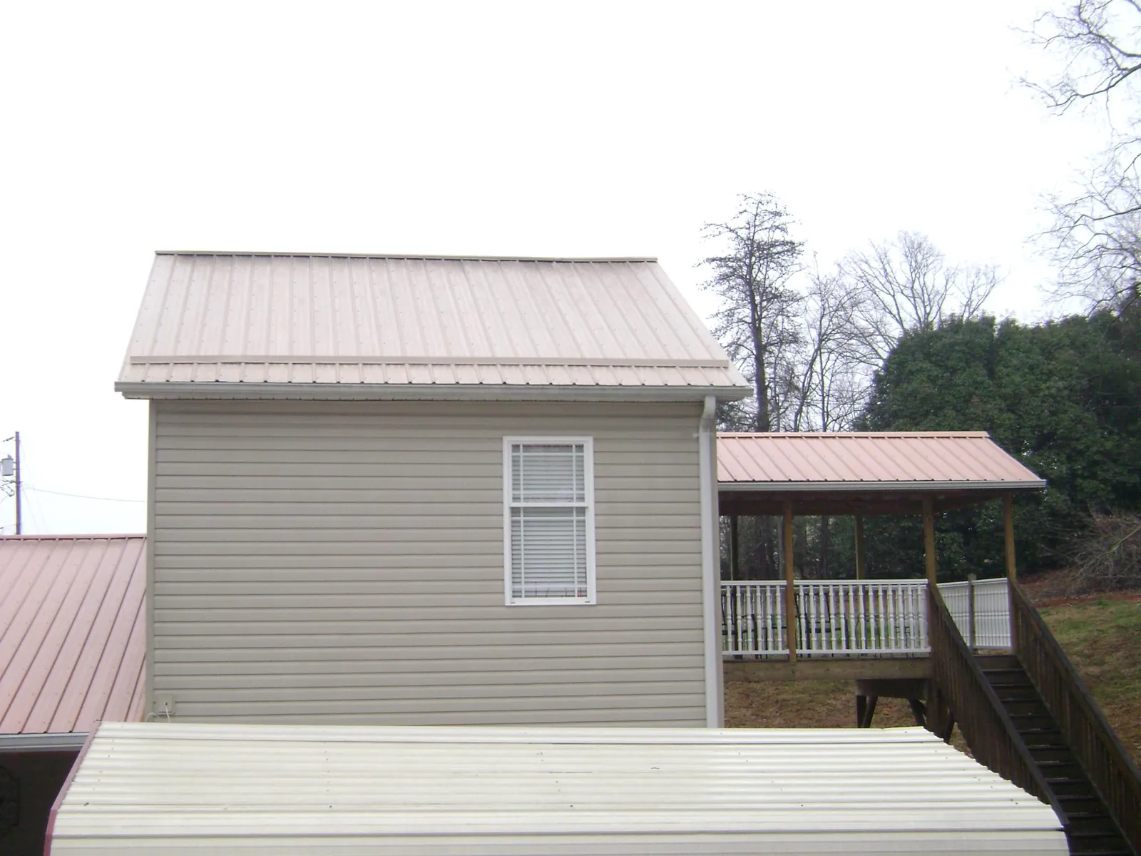 Tan metal roofs on a two story addition and attached porch, from a Roof Replacement job in Moroni